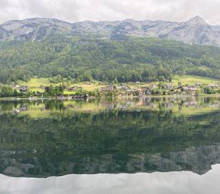 Bergsee im Vordergrund mit Alpendorf und Bergen dahinter